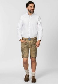 Leichtes weißes Hemd mit Knopfverschluss, kombiniert mit tanfarbenen Lederhosen, die mit dekorativen Stickereien, Taschen und traditionellen Lederschuhen versehen sind.