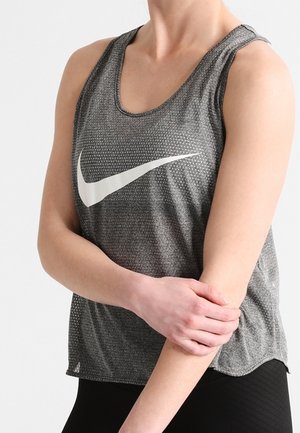 Persoon draagt een grijze mouwloze Nike sporttop en houdt zijn linker onderarm vast met zijn rechterhand tegen een effen achtergrond.