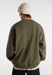 Groene sweatshirt met een ontspannen pasvorm, ronde halslijn en geribde manchetten, gelaagd over een lichtroze shirt, gecombineerd met donkere shorts.