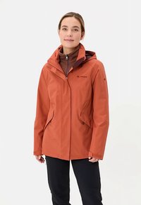 Giacca impermeabile rosso-arancione con cappuccio, chiusura frontale con cerniera e due tasche laterali. Presenta un logo e un interno morbido.