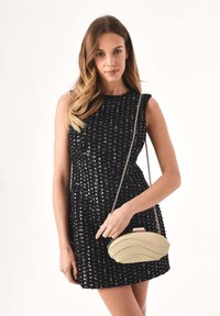 Abito nero in paillettes con silhouette aderente e dettagli sulle cuciture delle spalle, abbinato a una pochette color crema con texture ondulata.