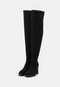 Bottes noires cuissardes en daim avec un talon épais, présentant une texture lisse et un design minimaliste. Aucuns motifs ni accessoires visibles.