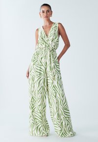 Tuta a righe verdi e bianche con design incrociato, senza maniche, cintura in vita e pantaloni a gamba larga. Tessuto leggero.