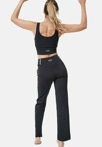 Zwarte atletische crop top en bijpassende high-waisted broek. Gladde stof, aansluitend ontwerp met gouden strepen aan de zijkanten, minimale branding.