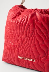 Piros bőr kézi táska, texturált, steppelt dizájnnal. Arany tónusú fémalkatrészekkel rendelkezik, elöl a "JUST CAVALLI" logóval.