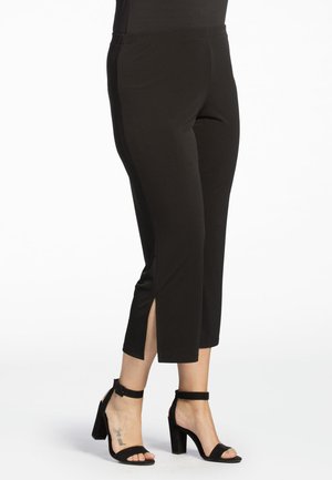 Pantalons noirs cropped en tissu lisse, avec des fentes sur les côtés et une taille élastique. Assortis à des talons hauts noirs avec bride à la cheville.