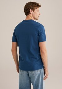 Sötétkék, rövid ujjú póló, puha pamutból készült, kerek nyakkivágással és laza fazonnal. Világoskék farmernadrággal viselve.