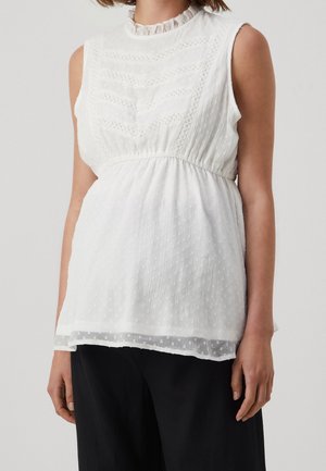 Biała bluzka bez rękawów z teksturowanej tkaniny, z falbankowym kołnierzem, koronkowymi detalami i marszczonym taliowaniem, noszona z czarnymi spodniami.