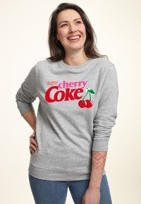 Felpa grigia con la scritta "Enjoy cherry Coke" in grassetto rosso e rosa, con grafica di ciliegie. Polsini e orlo a costine, tessuto di peso medio.