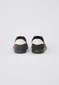 Sneaker scuri in suede con un accento bianco sul tallone e strisce rosse, bianche e blu sui lati. Suola in gomma e design a profilo basso.