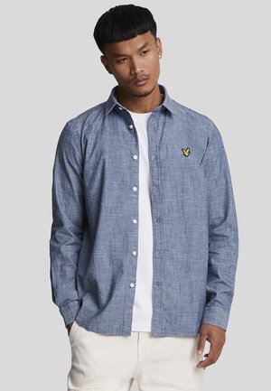 Chemise à boutons en chambray bleu clair, dotée d'un col pointu, de manches longues et d'un logo brodé jaune sur la poitrine.