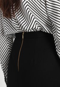 Svarta byxor med en gulddragkedja på baksidan, ihopparade med en långärmad topp i vit och svart randig design med en flödande stil.