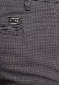 Pantaloni grigi con un motivo testurizzato, dotati di una tasca frontale e di un'etichetta nera rettangolare "GUESS" cucita.