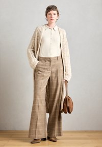 Beige gebreide cardigan, crèmekleurig overhemd met knopen en schoudervullingen, en bruine geruite wijde broek. Gecombineerd met een brownbag en enkellaarsjes.
