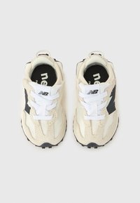 Hvite sneakers med mesh og semsket overmateriale med svarte detaljer, strukturert yttersåle og hvite lisser. Merkevarens logo er synlig på siden.