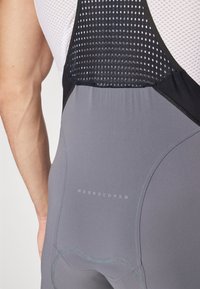 Gray cycling bib shorts feature a textured black mesh back panel, subtle branding, and smooth seams for comfort and fit.