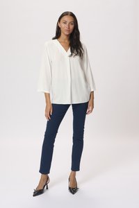 Witte blouse met een V-hals en driekwart mouwen, gecombineerd met donkerblauwe slim-fit broek en zwarte puntige hakken.