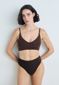 Barna bralette vékony pántokkal, V-kivágással. Magas derekú barna bikini alsó, enyhe fényléssel. Sima textúra.