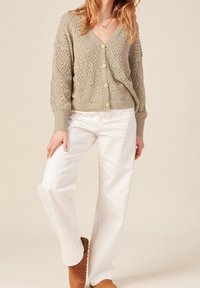 Sweter rozpinany na guziki w jasnym oliwkowym kolorze z wzorami rombów, z długimi rękawami; zestawiony z białymi spodniami o szerokich nogawkach i brązowymi kozakami.