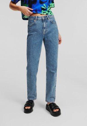 Jeans high-waisted de culoare albastru deschis, cu o tăietură dreaptă clasică, având cinci buzunare și o estompare subtilă. Asortați cu sandale negre masive.
