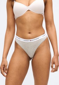 Szürke tanga fehér, "TOMMY HILFIGER" logóval ellátott derékpánttal. Az anyag sima textúrájú, minimalista kialakítású.
