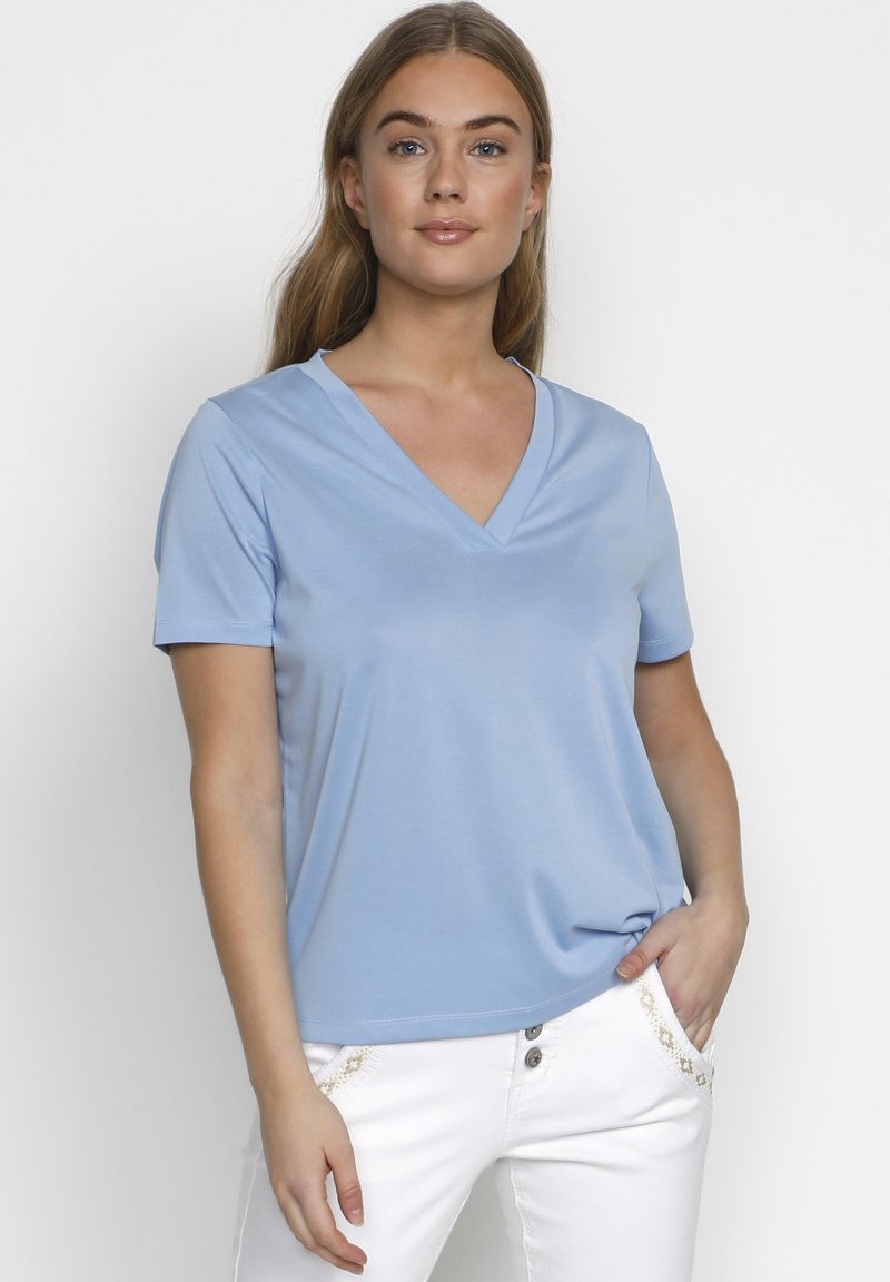 Lyseblå v-hals t-shirt med korte ærmer, blødt stof, afslappet pasform og subtil glans. Bæres med hvide bukser med dekorative detaljer.