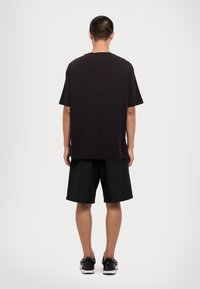 Tricou din bumbac negru, cu croială lejeră, mâneci scurte și tiv drept, asociat cu şorturi negre și adidași negri.