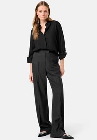 Schwarzes Leinen-Hemd mit Knopfleiste, kombiniert mit hoch taillierten schwarzen Hosen. Der Look zeichnet sich durch leicht aufgerollte Ärmel und spitze schwarze Ballerinas mit Verzierungen aus.