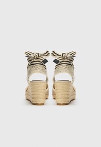 Kilehæl-sandaler med en vævet tekstiloverdel i beige og sorte striber, med en bueaccent og en vævet jutehæl; åben bagdesign.