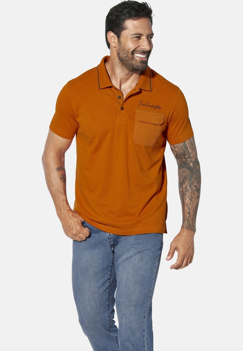 Orange polo shirt with a pocket, black stitching detail, short sleeves, and a fitted design, paired with blue jeans.