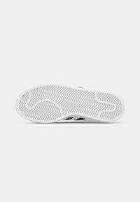 Semelle d'une sneaker blanche avec un motif de bande de roulement en zigzag, vue de dessous sur un fond clair.