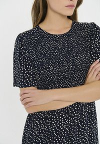 Námornícky šaty s bielym bodkovaným vzorom, krátkymi rukávmi, detailmi so zberaným živôtikom a voľným strihom. Materiál pôsobí ľahko a štruktúrovanie.