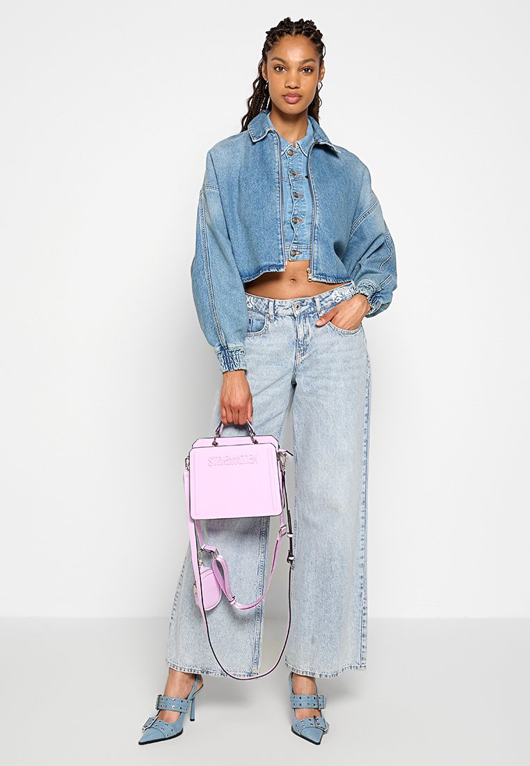 Veste en jean courte avec des manches bouffantes, jean large taille haute bleu clair, sac à main rose pastel et mules à talons bleues avec des brides.