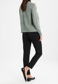 Šedé tričko s dlouhým rukávem a texturovaným povrchem, spárované s černými zúženými kalhotami a plochými černými botami. Outfit má neformální vzhled.