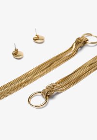 Gold jewelry set featuring textured, woven mesh chain bracelet with a looped knot detail and small matching circular stud earrings.