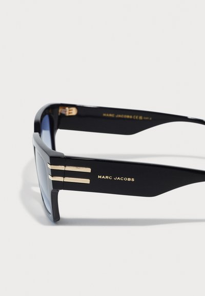 Gafas de sol negras con montura rectangular, que presentan franjas doradas en las patillas. La marca "MARC JACOBS" está exhibida en letras doradas.