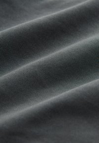 Tissu gris foncé avec une texture diagonale fine côtelée, présenté en gros plan sur des plis avec un éclairage doux.