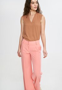 Brązowy bezrękawnik z dekoltem w serek i kieszenią, zestawiony z różowymi spódnicami o wysokim stanie i szerokich nogawkach, które mają dwa guziki.