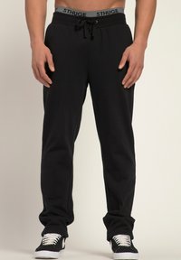 Svarta sweatpants med snörning i midjan, elastiska manschetter vid anklarna och en synlig grå logotyp på midjebandet. Material i bomullsmix.
