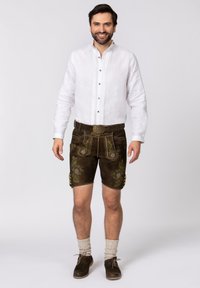 Braune Lederhosen mit grüner Stickerei, kombiniert mit einem weißen Leinenhemd und hellgrauen Kniestrümpfen. Braune Schuhe vervollständigen das Outfit.