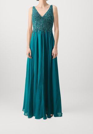 Frau trägt ein ärmelloses, türkisfarbenes bodenlanges Kleid mit einem perlenverzierten, strukturierten Oberteil und einem fließenden Chiffonrock.
