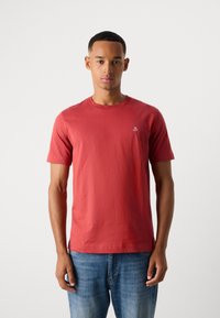 Camiseta de algodón roja con mangas cortas, cuello redondo y un pequeño logo bordado en el lado izquierdo del pecho. Textura suave, corte casual.