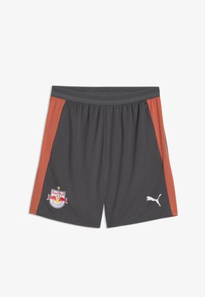 Pantalones cortos deportivos de color gris oscuro con paneles laterales color óxido, logo de Red Bull Salzburg en la pierna izquierda y logo blanco de Puma en la pierna derecha.