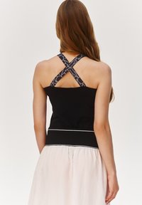 Czarny top bez rękawów z krzyżującymi się czarnymi i szarymi paskami, połączony z jasnoróżową spódnicą z kontrastowym pasem w talii.