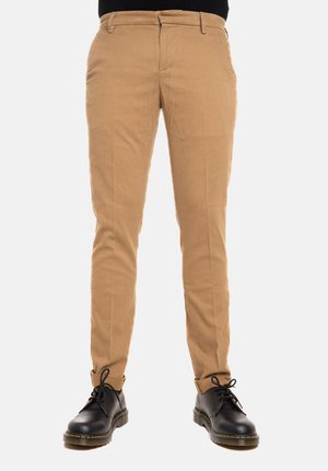 Chinos khaki con vestibilità slim, dotati di tasche laterali e passanti per cintura, abbinati a stivali neri con lacci, che mettono in evidenza una trama liscia e linee pulite.