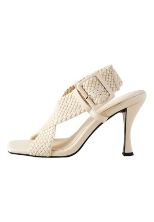 Beige high-heeled sandal with woven strap design, square toe, and adjustable buckle. Features a slender heel and smooth texture.