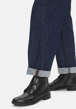 Czarne skórzane botki na sznurowadła z metalowymi oczkami, połączone z ciemnoniebieskimi dżinsami z podwiniętymi mankietami w jasnoniebieskim kolorze.