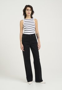Svarta högmidjade jeans med rak bendesign, parat med en vit linne med svarta horisontella ränder. Slät tygtextur.