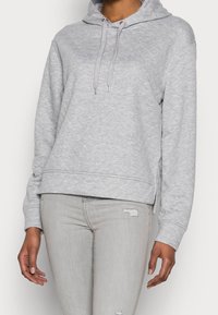 Grå huvtröja i quiltad textur, med dragsnören, ribbade mudd och sidofickor. Återförenad med ljusgrå slitna jeans.