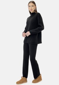 Sort ribstrikket sweater og matchende bukser med høj hals og lange ærmer. Beige ankelstøvler fuldender outfittet.